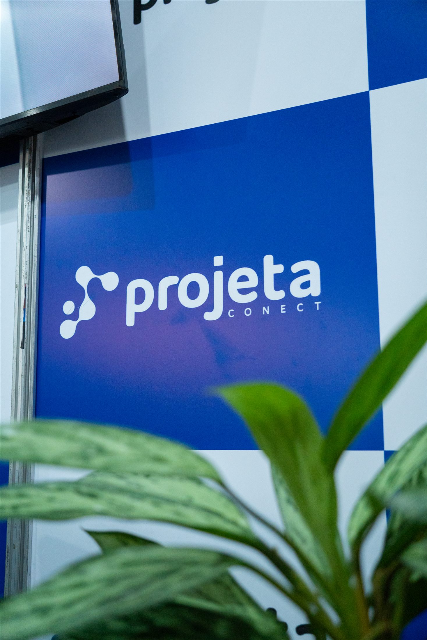 Logo da Projeta Conect no estande da feira com plantas em primeiro plano